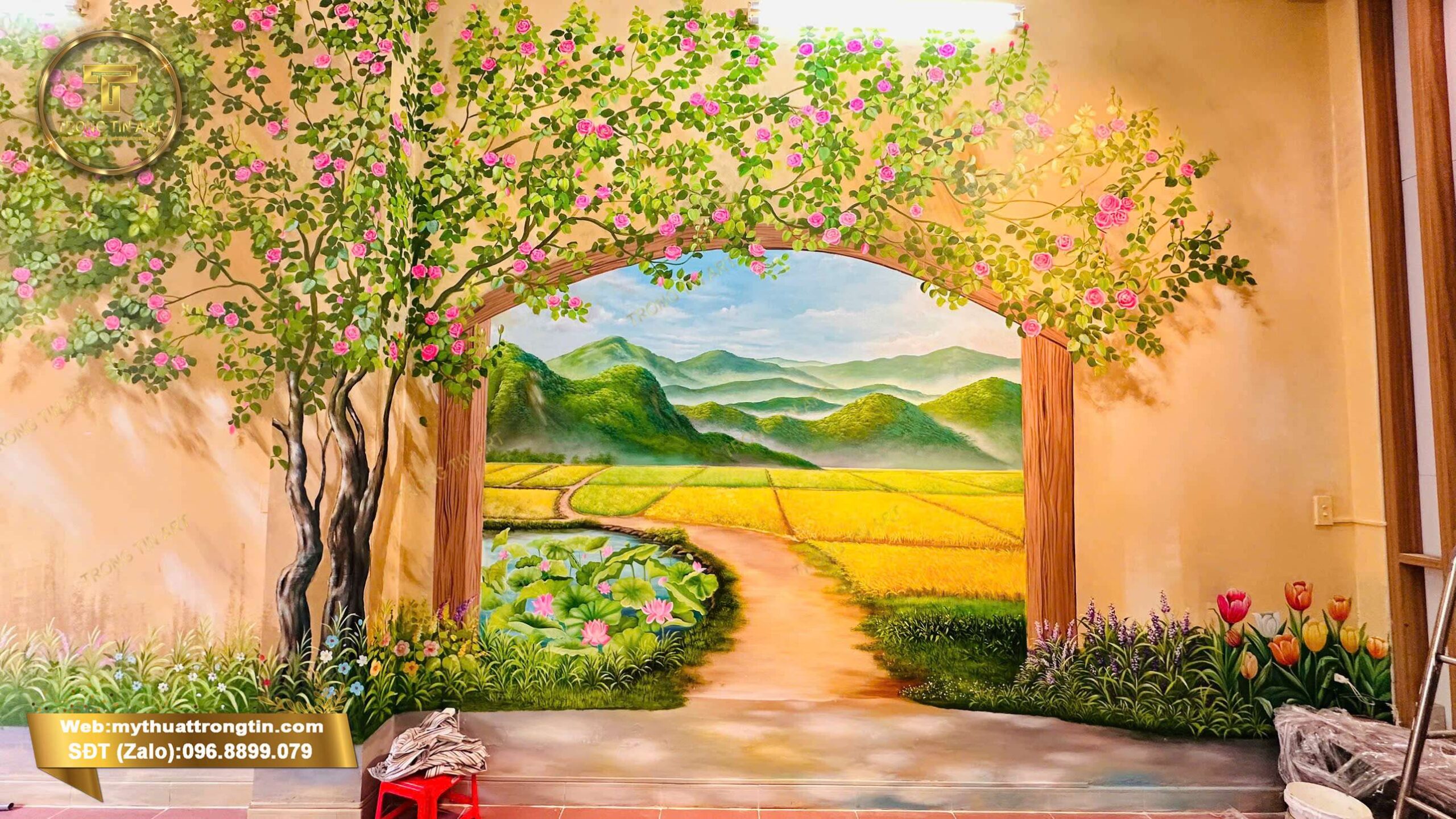 Vẽ tranh tường phong cảnh 3D đồng quê với cánh đồng lúa, cổng vòm hoa và núi non, thi công bởi Mỹ thuật Trọng Tín tại quán cà phê.